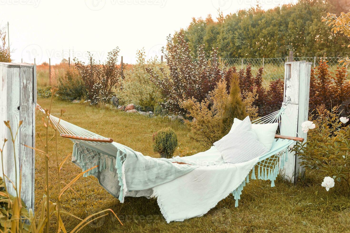 A hammock with pillows and a blanket on the street in the courtyard of a village house. A place to relax in the country. The concept of autumn photo