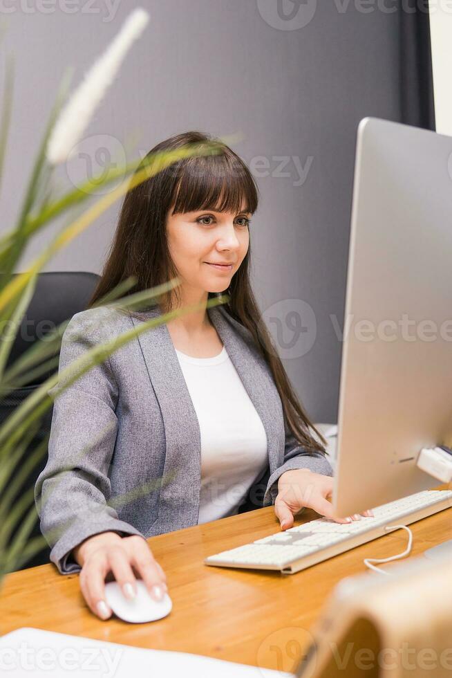 A brunette woman at a computer in the workplace. Business concept. photo
