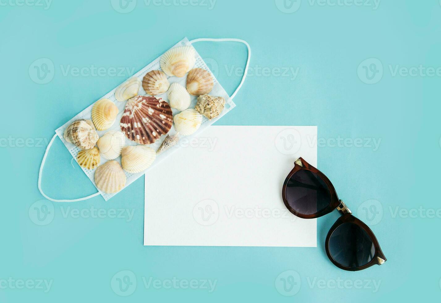 Medical face mask, sunglasses and seashells on a blue background. Flat lay, copy space, vacation cancellation, pandemic, tourism. photo