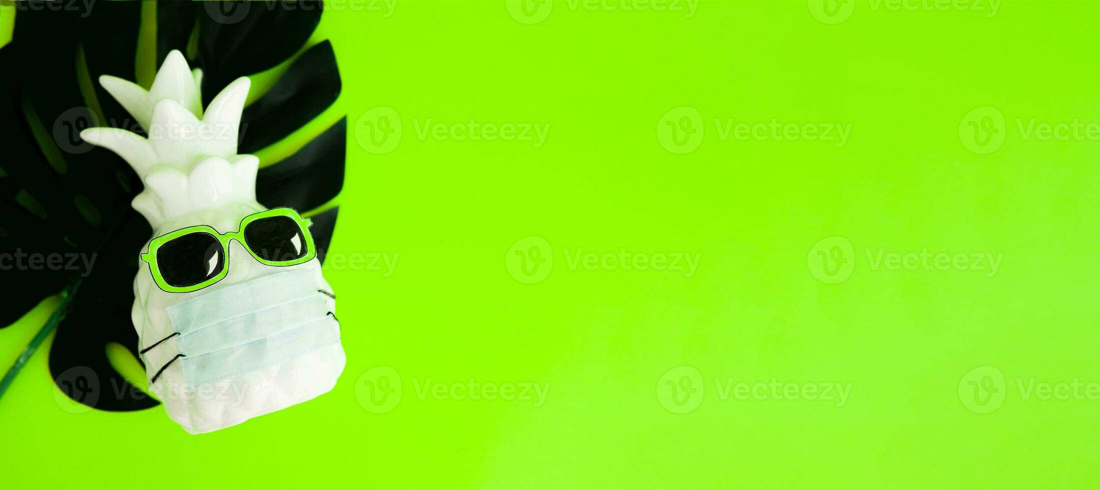 Pineapple in a medical mask and sunglasses on green neon background. Summer concept. Summer in Covid-19. Vision for the summer of 2020 during the coronavirus pandemic. photo