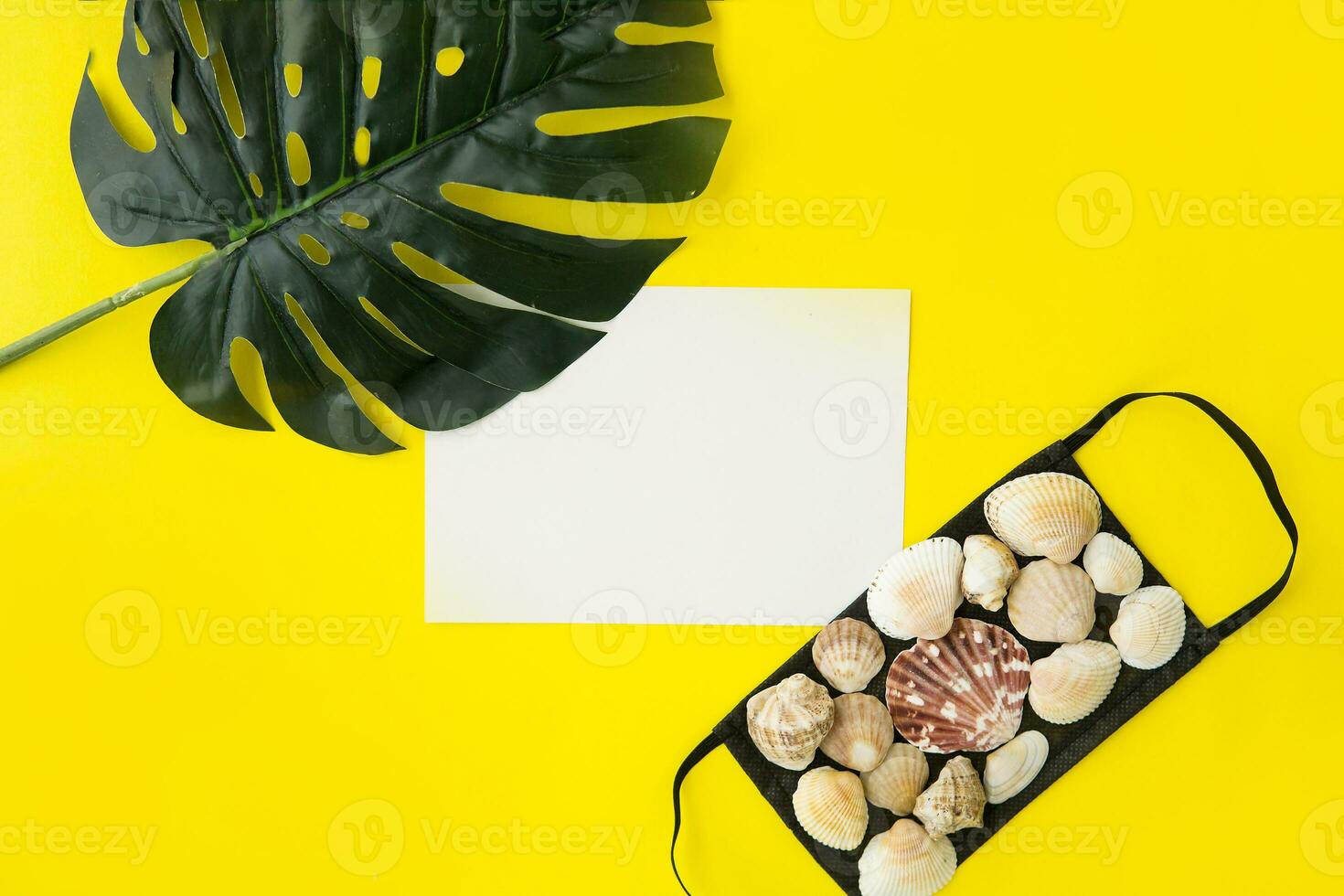 Black medical face mask and seashells, monstera leaf on a yellow background. Flat lying, copy space, vacation cancellation, pandemic, tourism. photo