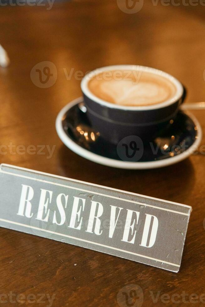 Coffee cup with a heart pattern in a blue cup on a wooden background. A sign with the inscription - reserved. photo