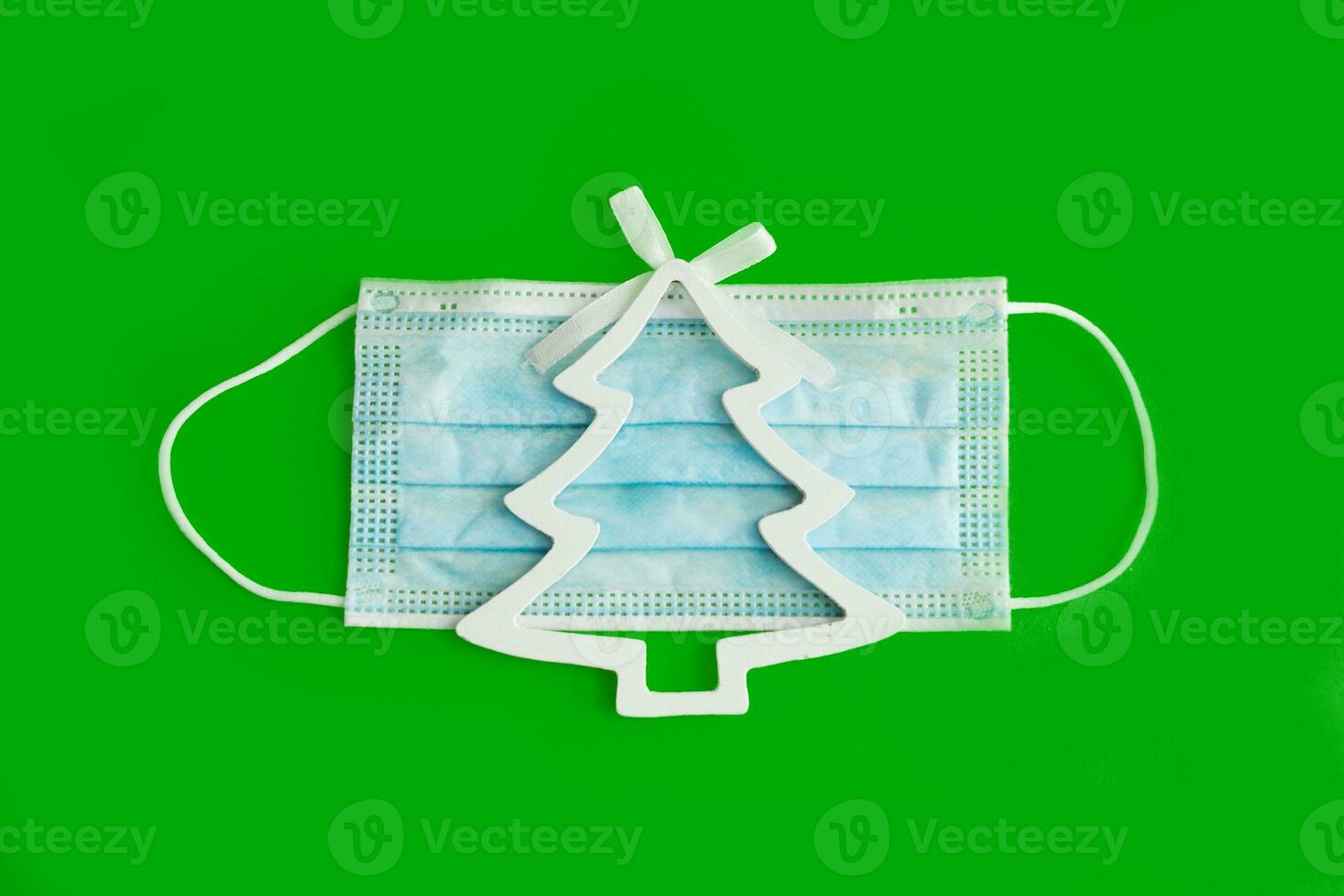 Christmas decorations decorative background. Decorative Christmas tree on a medical mask on a green background top View, minimalism, flat layout. Christmas and New year 2020. The Age Of Coronavirus. photo