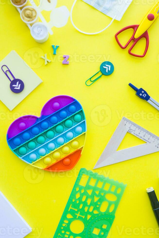 Close up of stationery and silicone toy popit. Flat lay composition. Yellow background. Space for text. Back to school photo