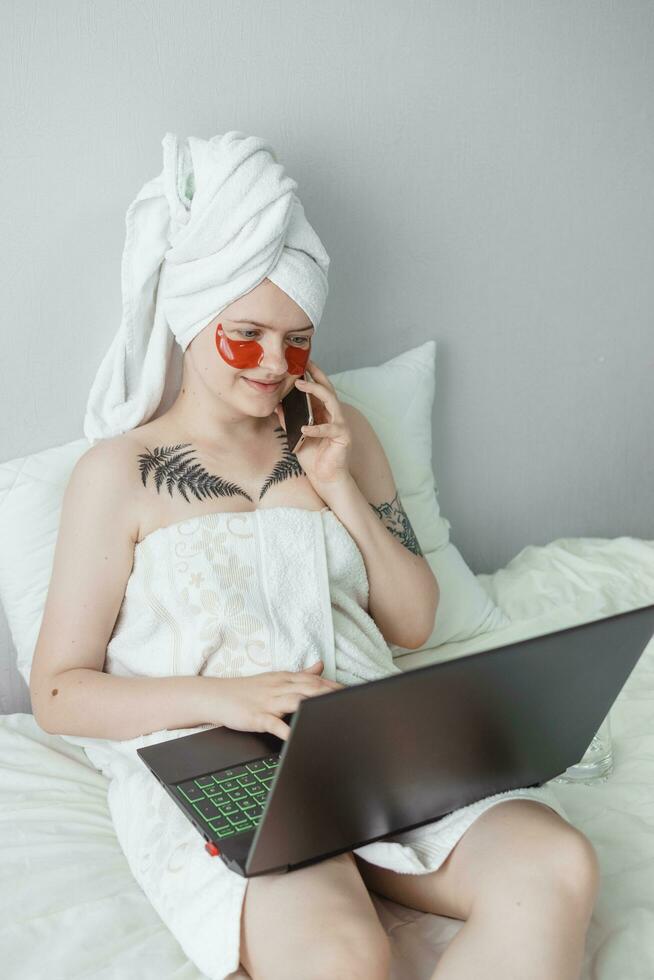 Tver, Russia-august 2, 2021 A woman after a shower is lying on the couch with a laptop and an eye mask at the same time. The concept of multitasking in the twenty-first century. photo