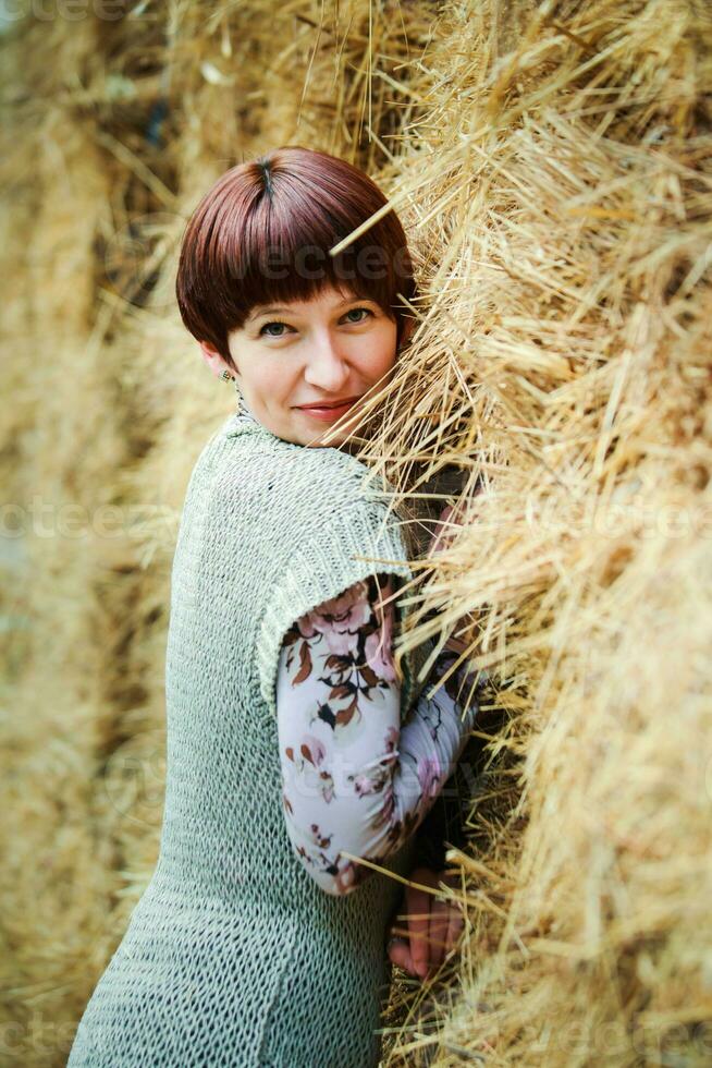 Beautiful woman with short hair looks into the frame. Portrait of a thirty-year-old woman. A girl in a stable in the background of haystacks. photo