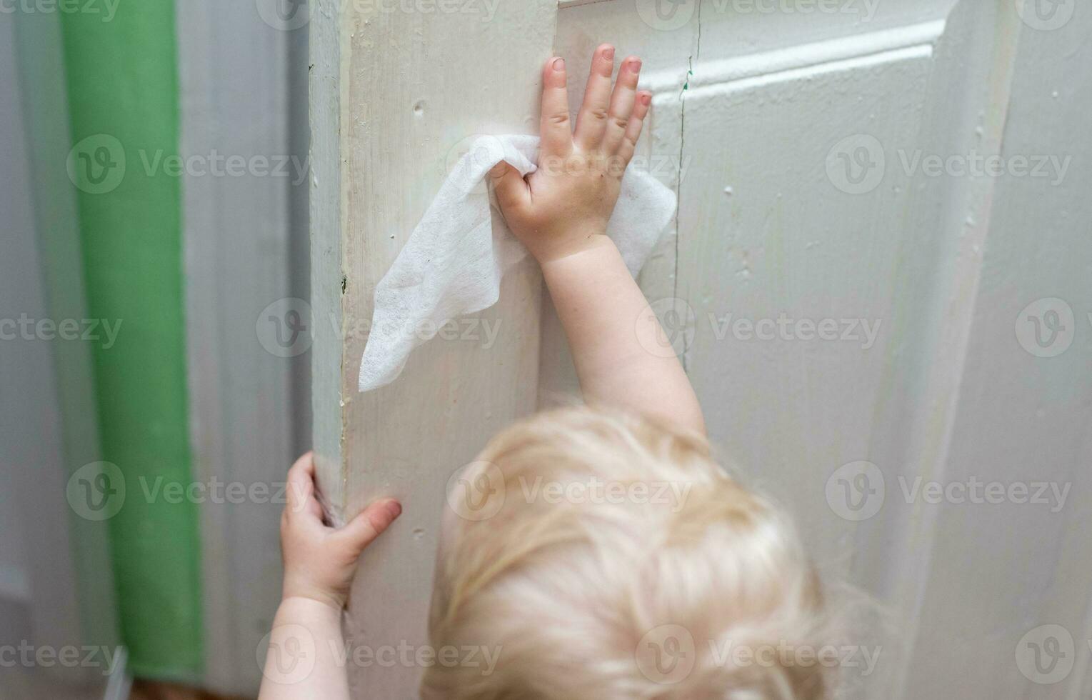 baby washes the vintage old doors with napkin during a viral epidemic. Cleaning home. Teaching children to be independent. use of wet wipes in everyday life photo