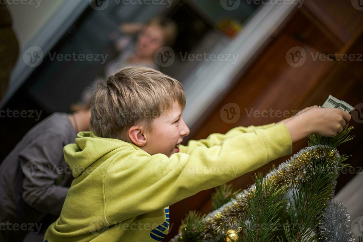 Boy clings a red ball on a branch of a Christmas tree at home. Preparing for Christmas at home. Real people. Decorating Christmas tree with a variety of toys photo