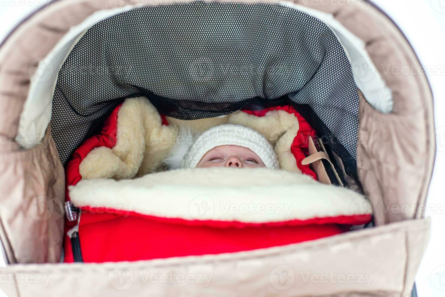 Baby sleeping in stroller in warm red envelope in winter outdoors photo