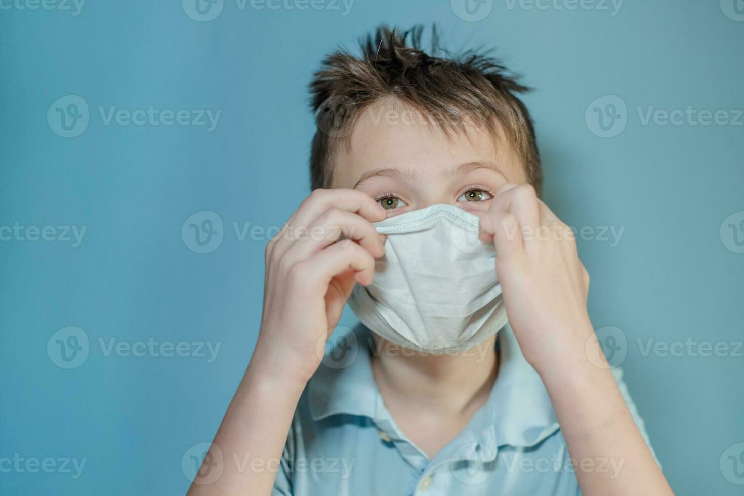 boy adjusts protective medical mask on face. Mistakes in dressing the mask. child touches face and carries virus. child with influenza or cold protected from viruses among patients with coronavirus photo