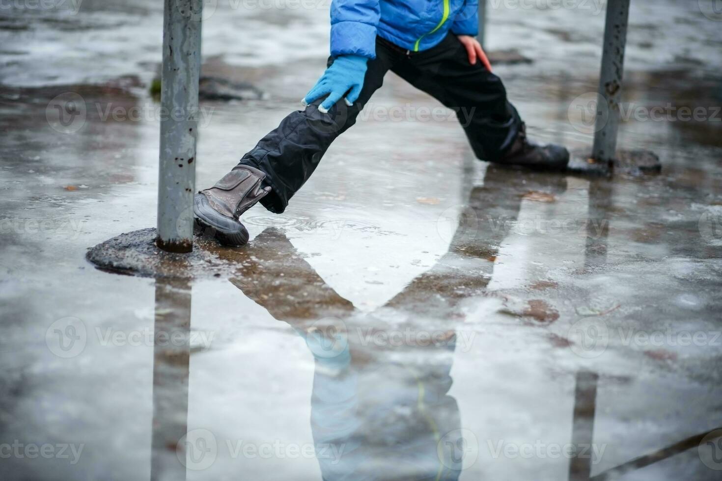 A child in snowboots boots is standing in a puddle of melted snow. Ice on the roads in the city. Not cleaned from snow and ice territory. Wet feet in winter. photo