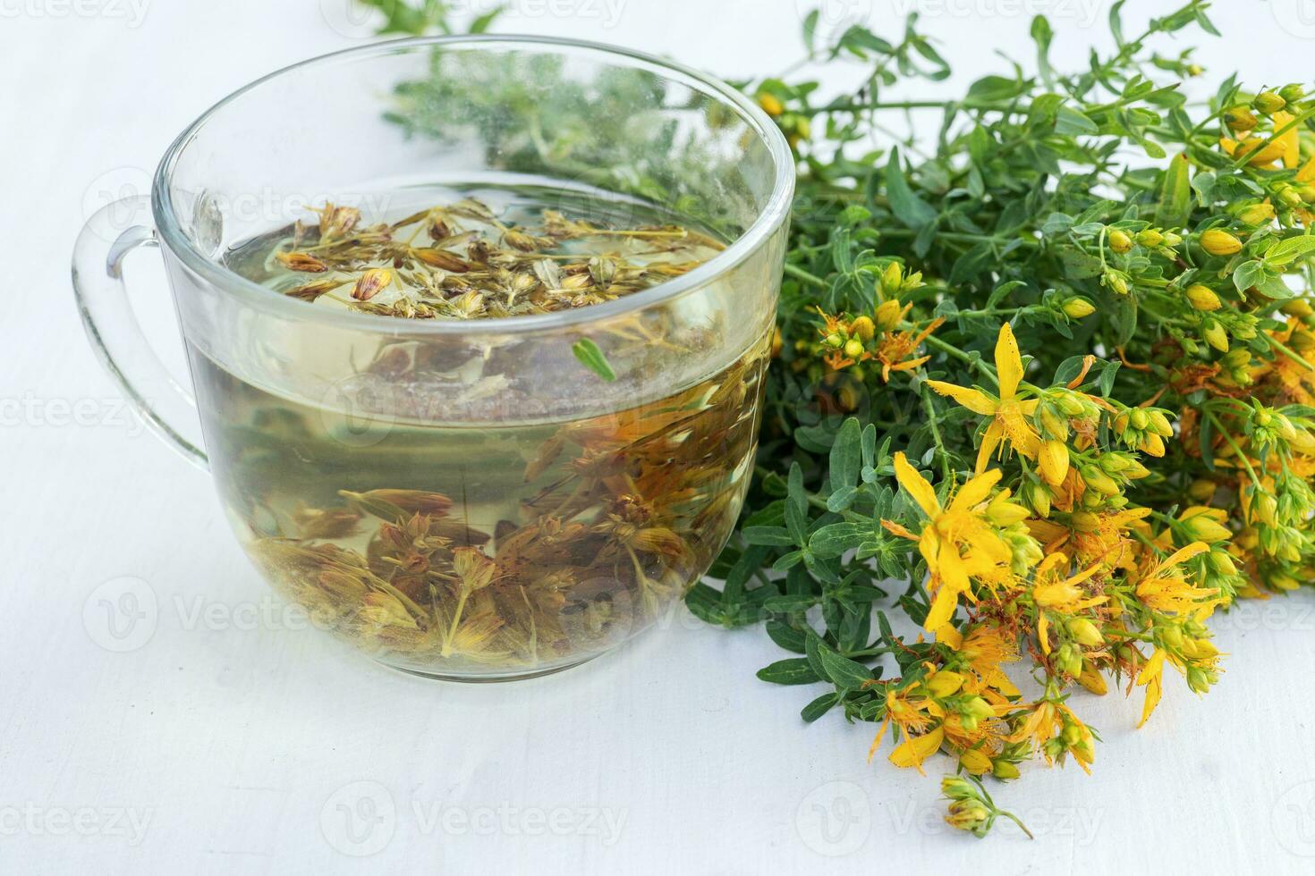 Transparent cup of St. John's wort remedy beverage with bunch fresh Hypericum yellow flowers. jar of spring honey. Medicinal herbs for Alternative Medicine and Homeopathic Remedies photo