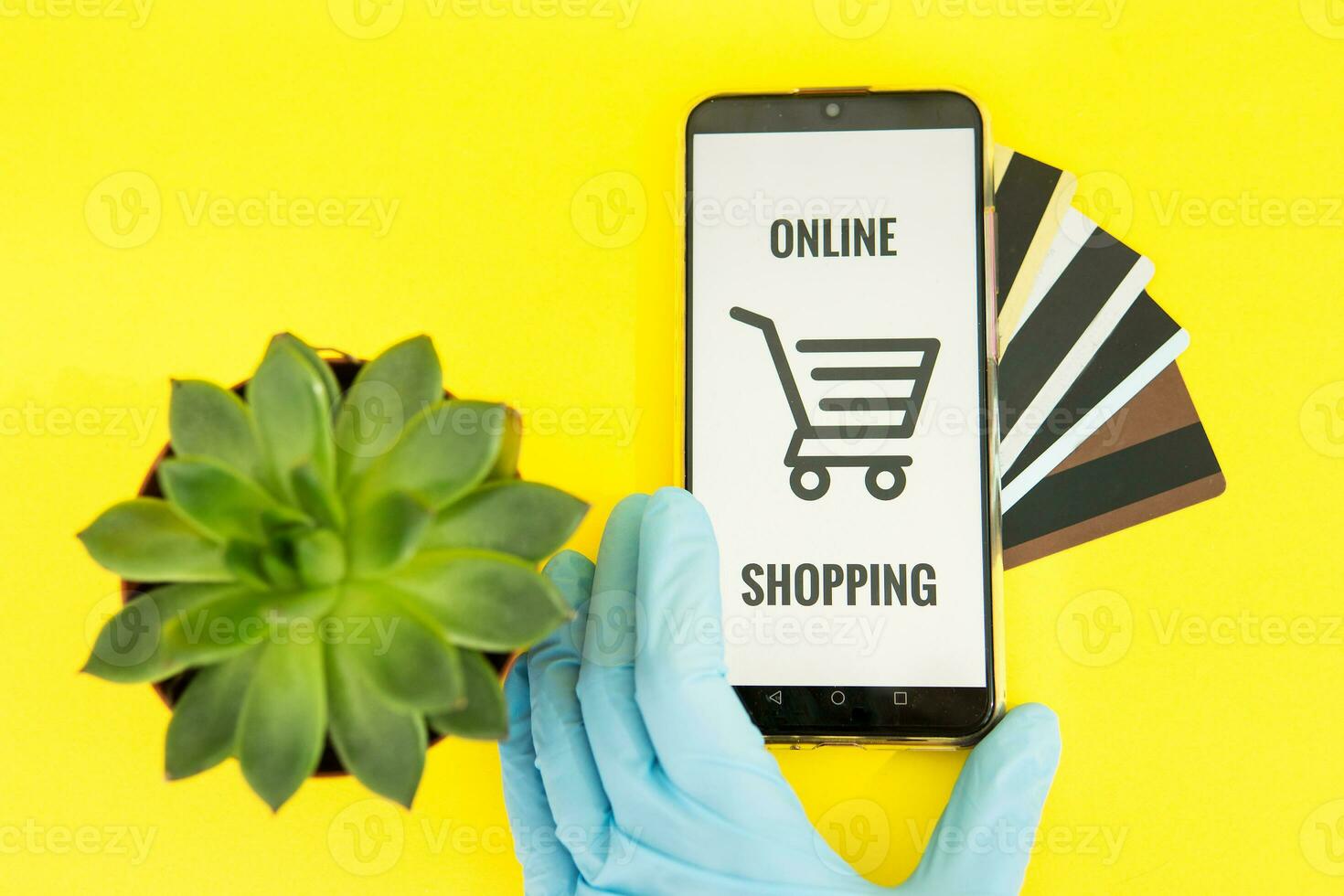 Close-up of hands in medical gloves with a smartphone. Online shopping, online banking, online payment. Payment with plastic cards. Flat Lay on a yellow background. photo