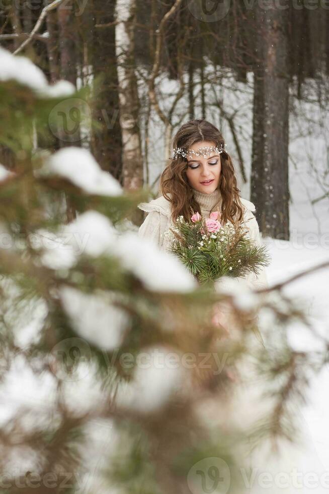 Beautiful bride in a white dress with a bouquet in a snow-covered winter forest. Portrait of the bride in nature. photo