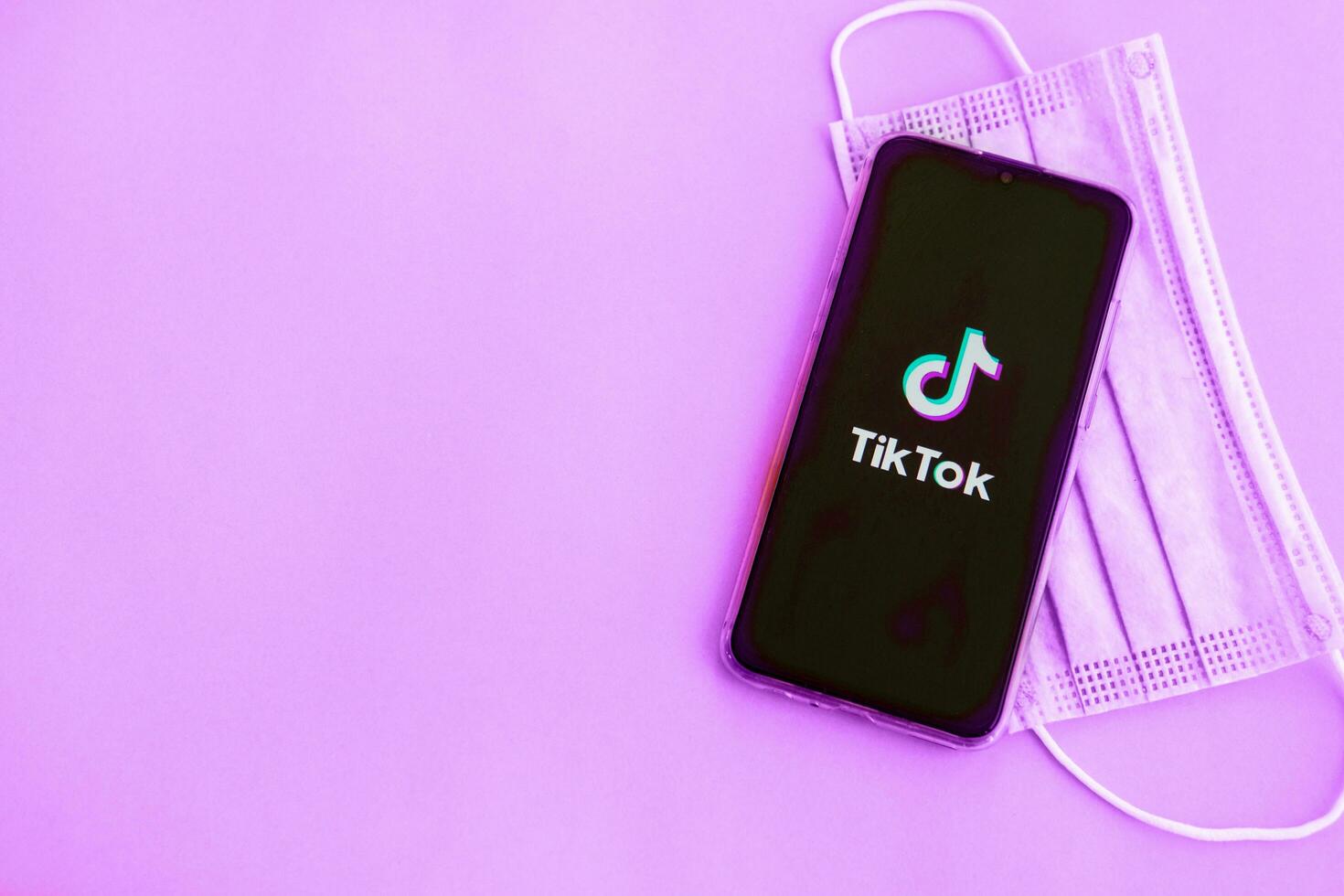 Tver, Russia - September 19, 2020. Tiktok app on the smartphone screen and medical protective mask on a lilac background. TikTok is a popular video sharing social network owned by ByteDance. photo