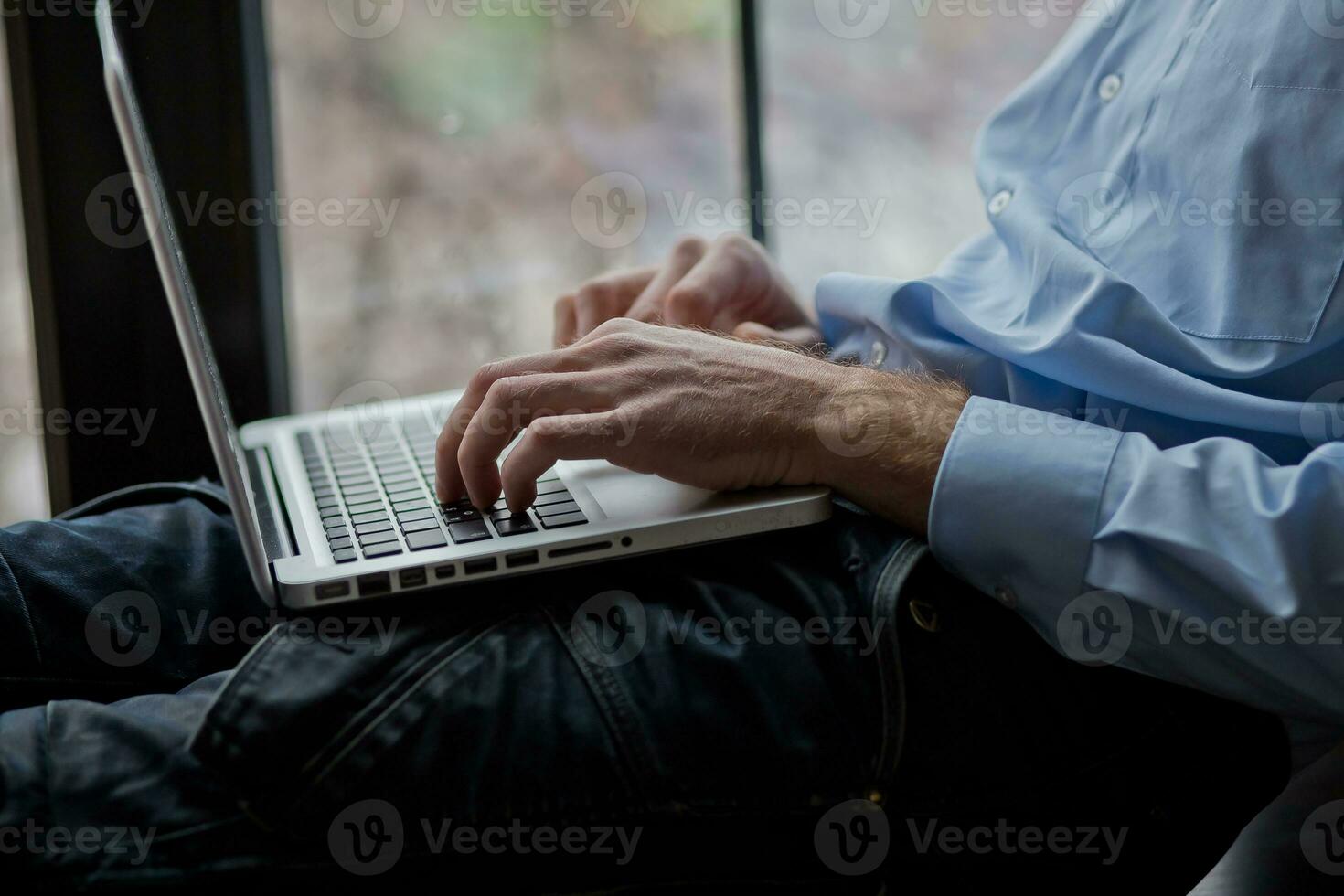 A man sits on a windowsill and works on a laptop. Beautiful man's wrist. Long fingers of a young man. photo