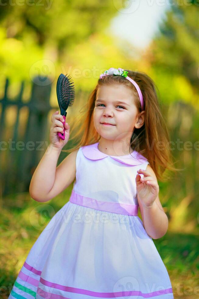 hermosa niña con largo pelo cardado trenzas. un niño participación un peine para el cabello. bueno niño camina en el tribunales en contra el antecedentes de el cerca. foto