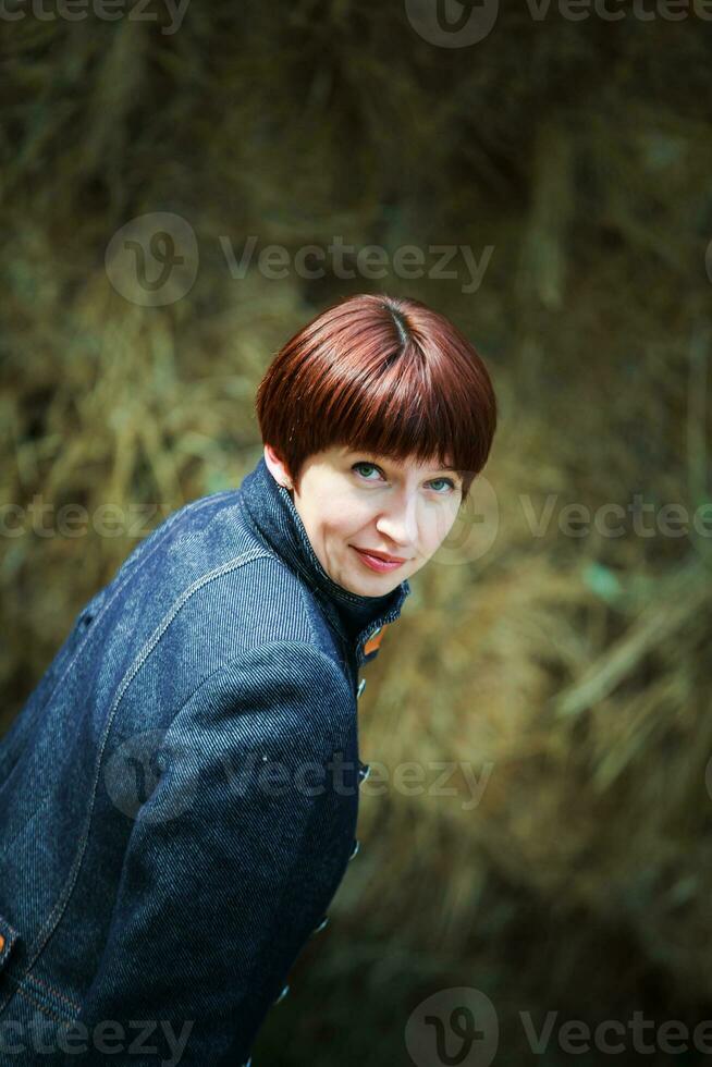 Beautiful woman with short hair looks into the frame. Portrait of a thirty-year-old woman. A girl in a stable in the background of haystacks. photo