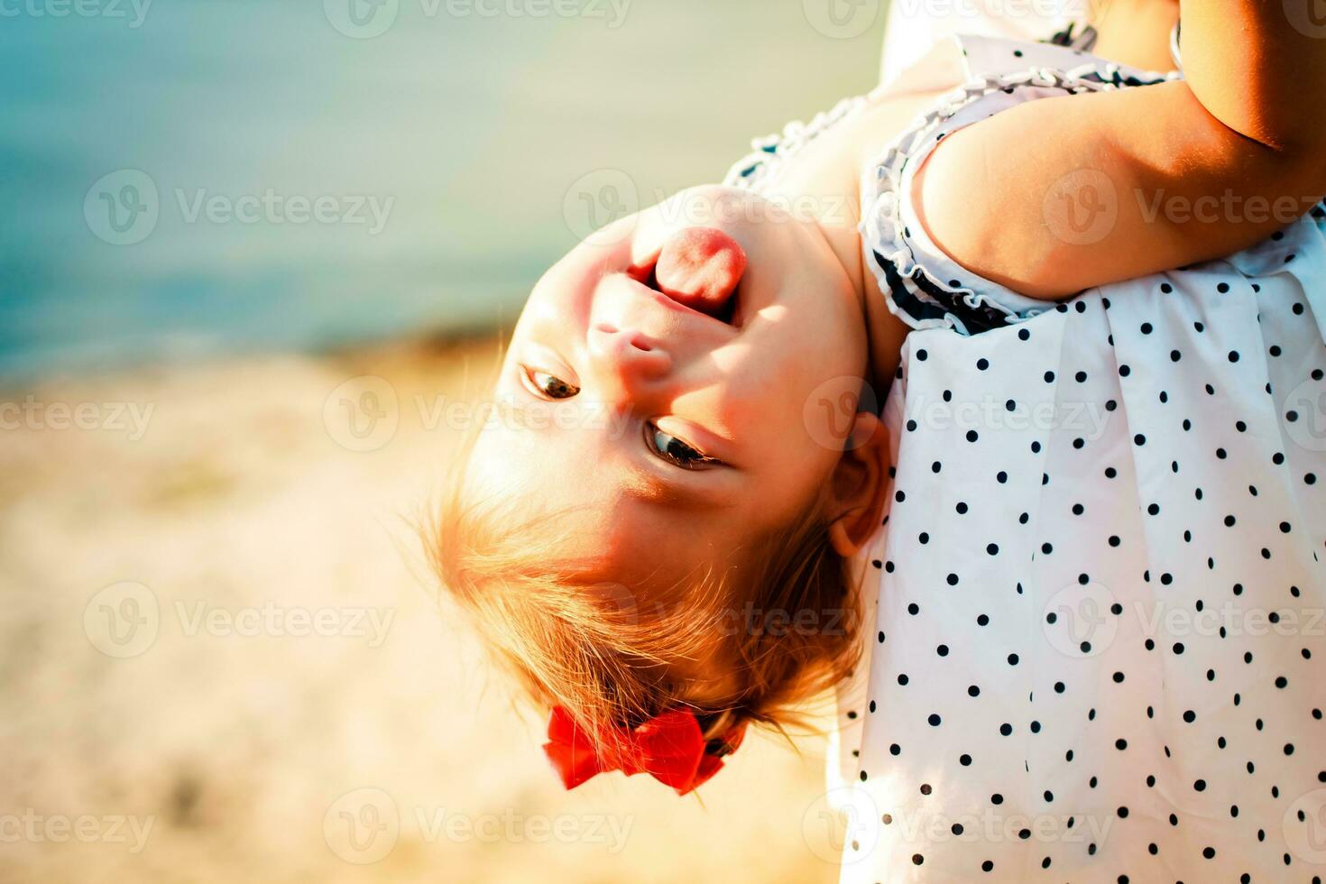 The little girl shows tongue. A child playing on the beach. Mom and baby are resting on the beach. Place for text. photo