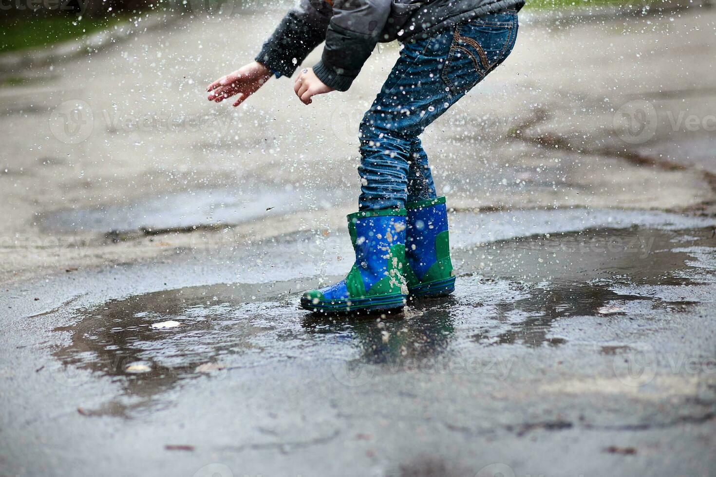 Boy in blue with green rubber boots jumped into deep puddle. photo