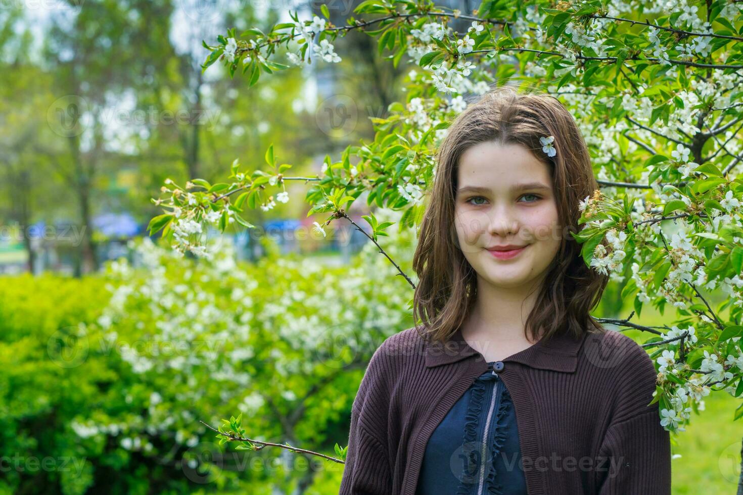 Beautiful girl among cherry flowers in spring. Portrait of a girl with brown hair and green eyes. photo