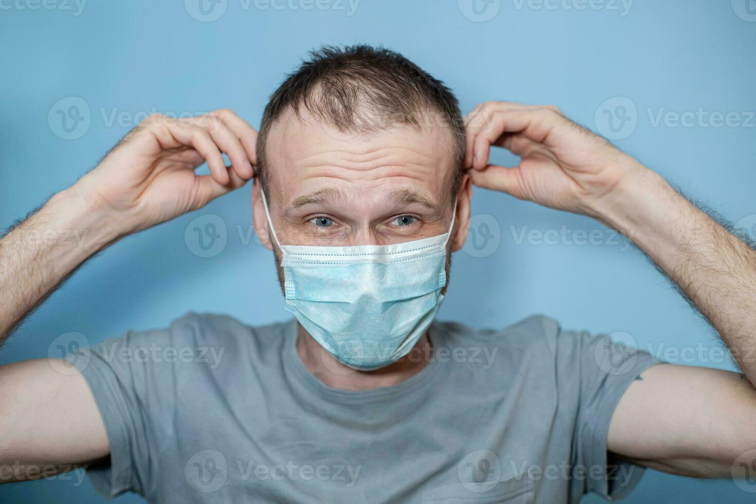 Man 40 wears ear loop protective mask. Angry man on blue background. hild with flu, influenza or cold protected from viruses among patients with coronavirus photo