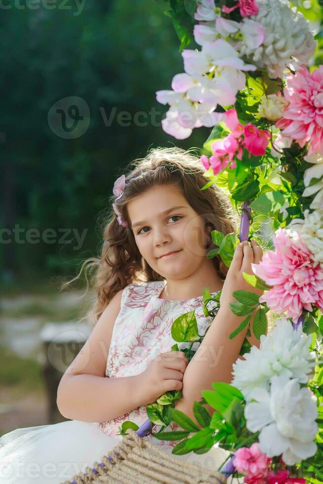 Beautiful caucasian girl sitting on beautiful swing with the colorful roses flower in the nature garden hanging on pole photo