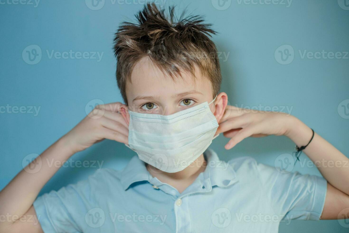 boy wears protective medical mask on face. child tucks the gum behind ears from mask. child with flu, influenza or cold protected from viruses among patients with coronavirus photo