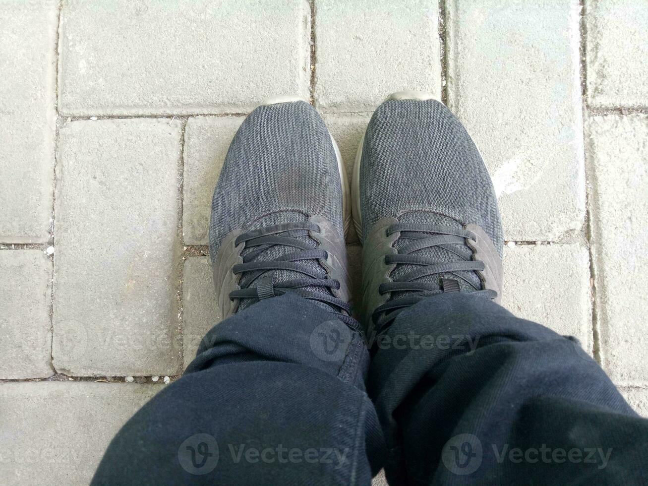 a pair of black shoes on brick paving, wearing black trousers, photographed from above photo