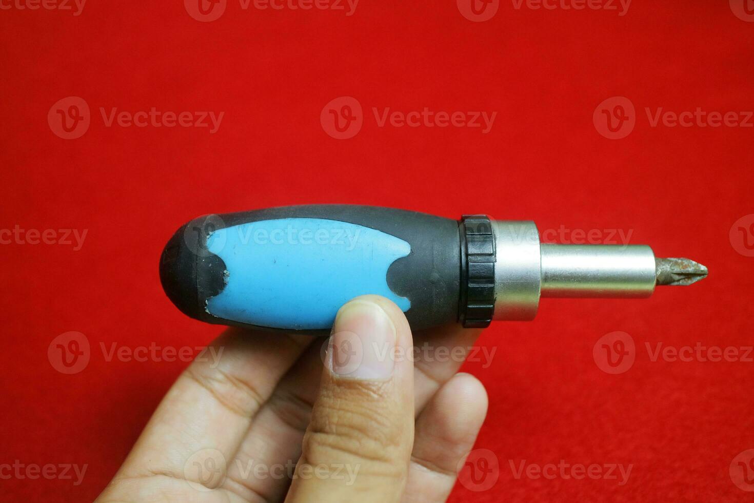 A hand holding a Mini stainless steel screwdriver with black and blue handle, on a red background photo