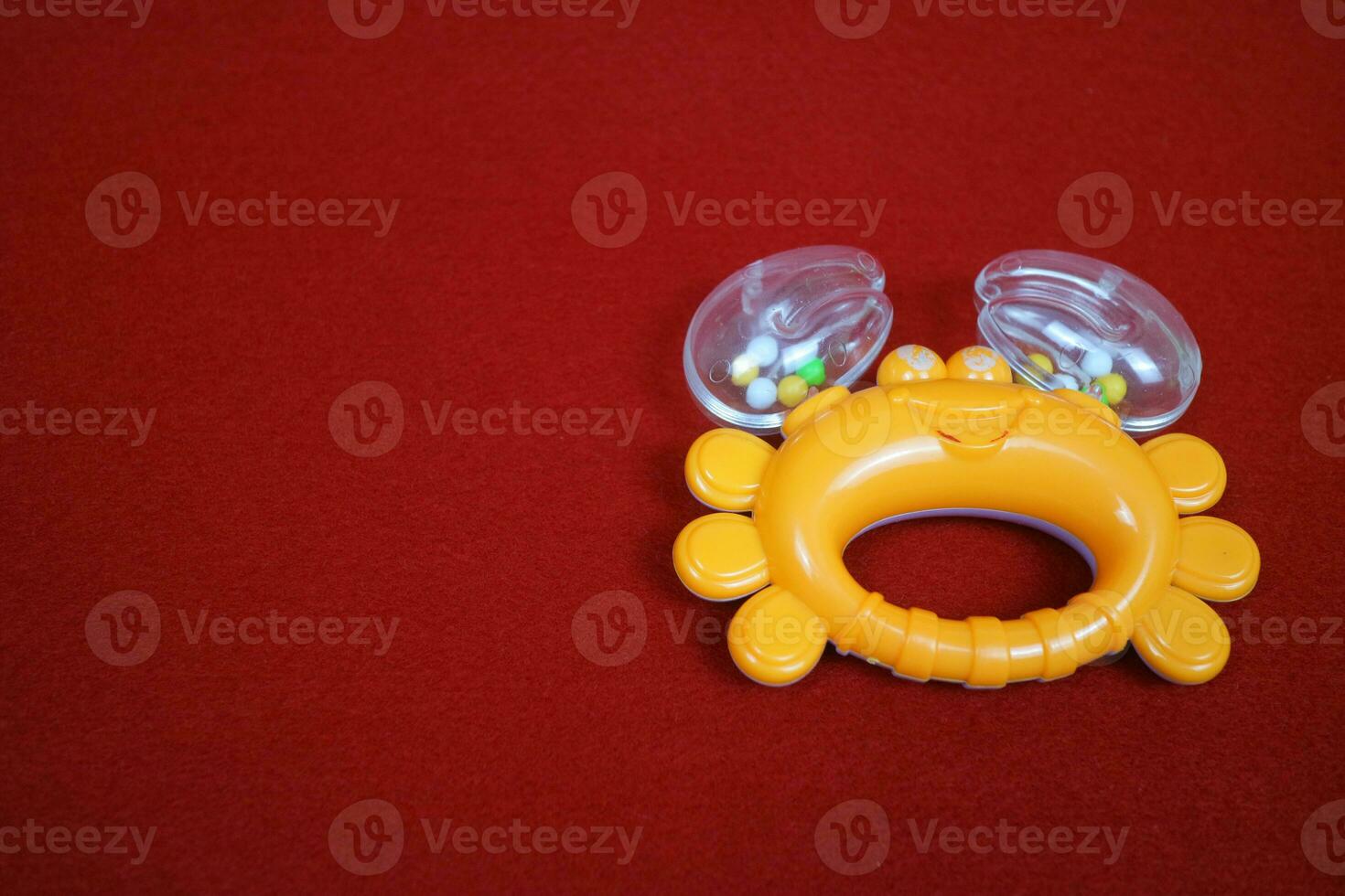 Yellow crab shaped children's toy, with small balls inside, makes a loud sound. On red background photo