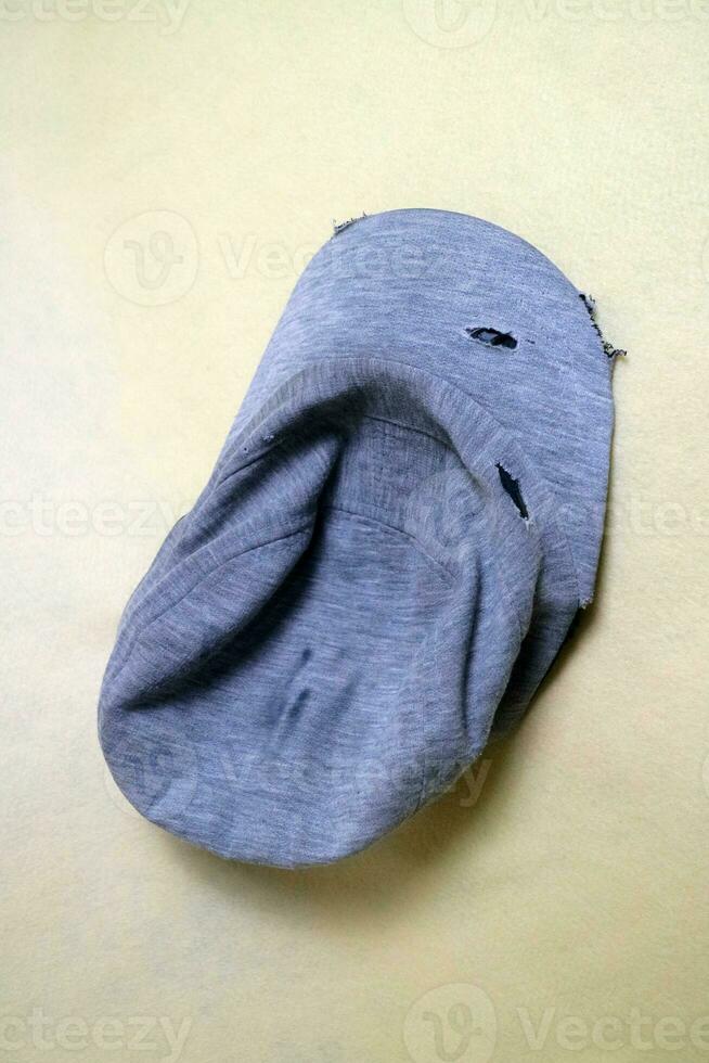 The gray cloth hat is in a worn condition with several tears. Cream background photo