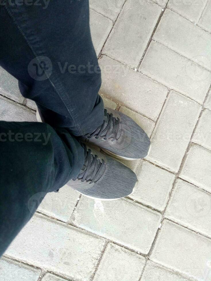 a pair of black shoes on brick paving, wearing black trousers, photographed from above photo