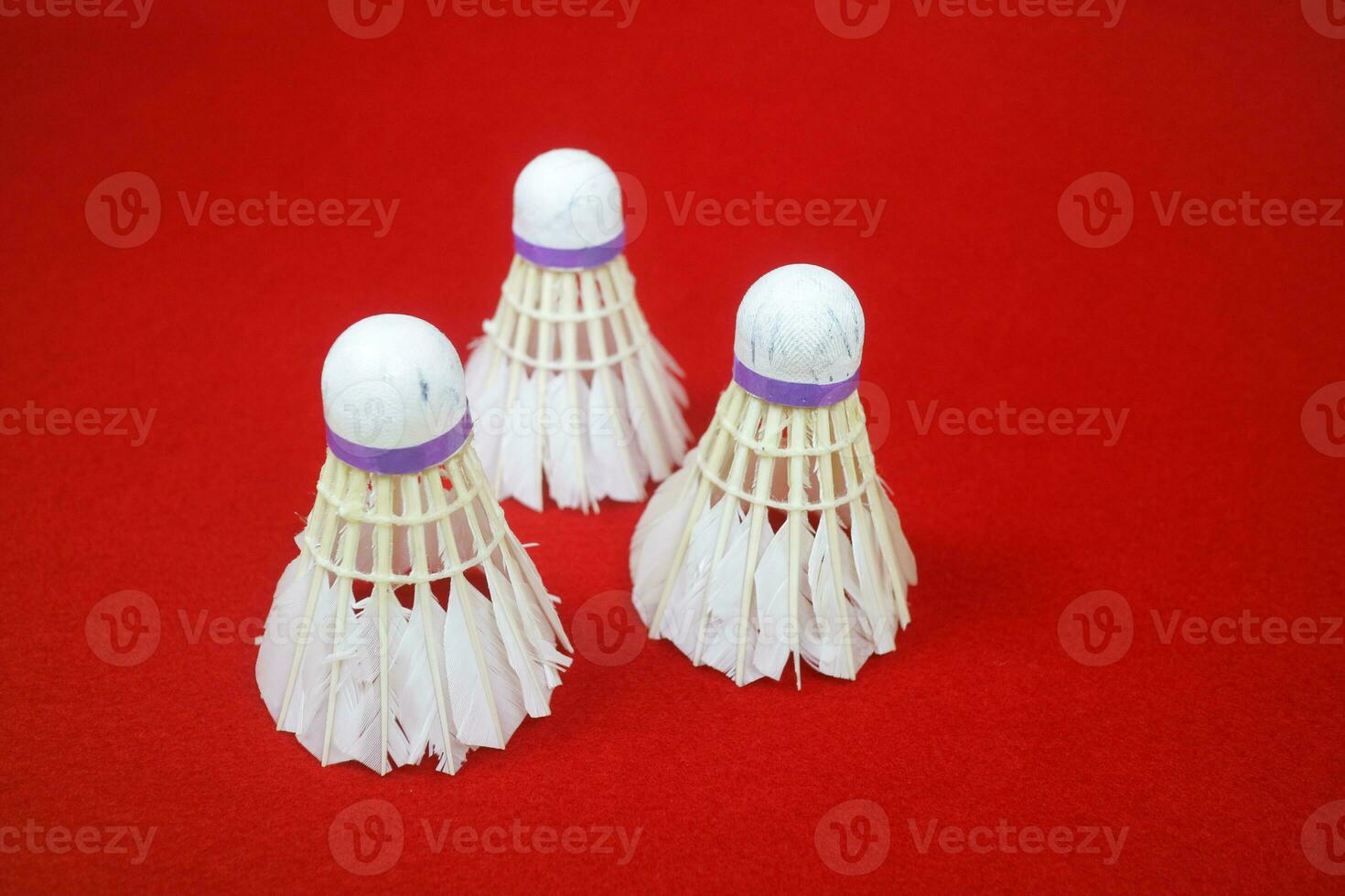 some used shuttlecocks, made of goose feathers, with purple ribbons on red background photo