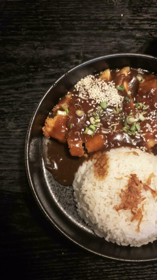 Flat lay of katsu don, black plate, black wood table photo