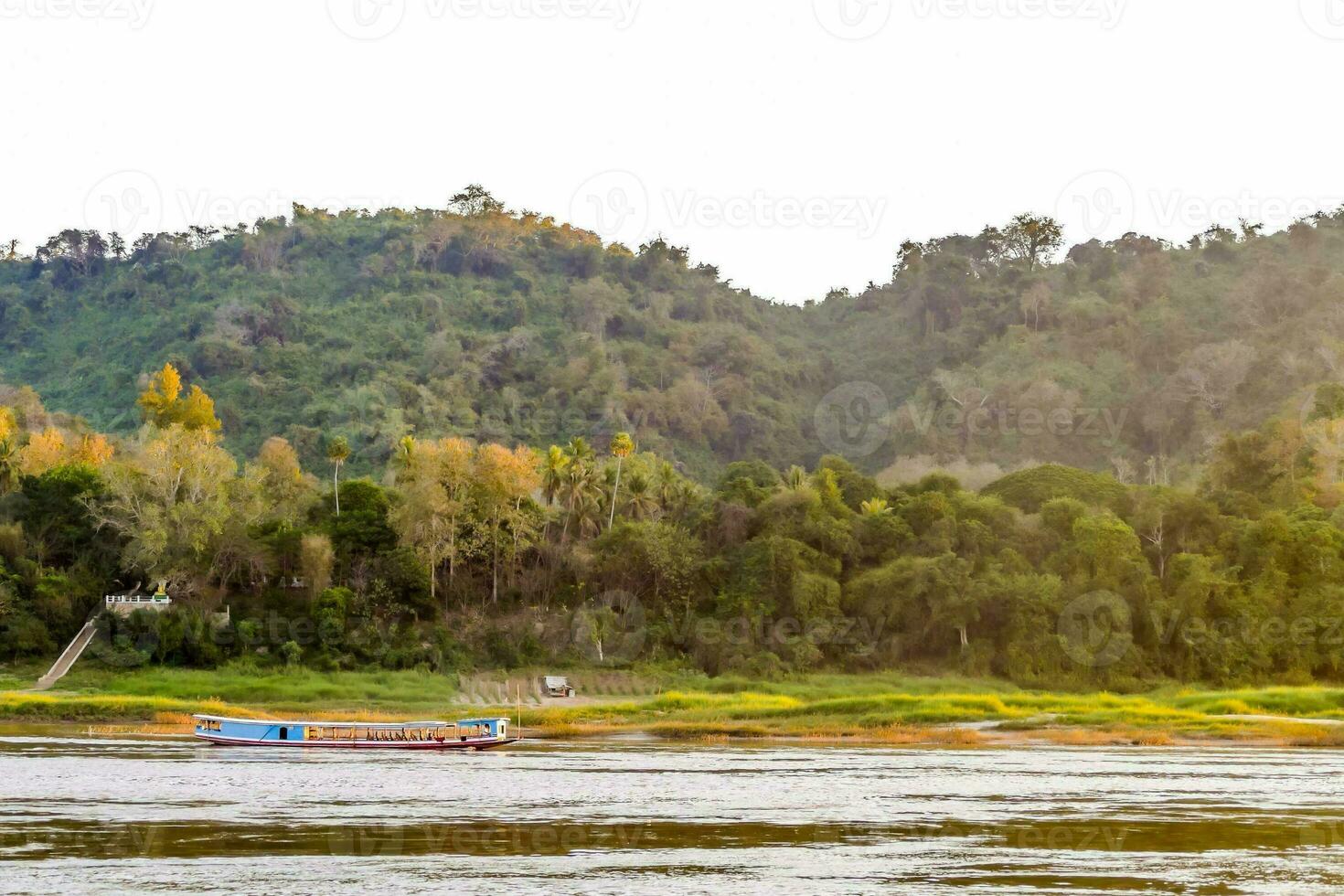 a boat is traveling down the river in front of a forested hill photo