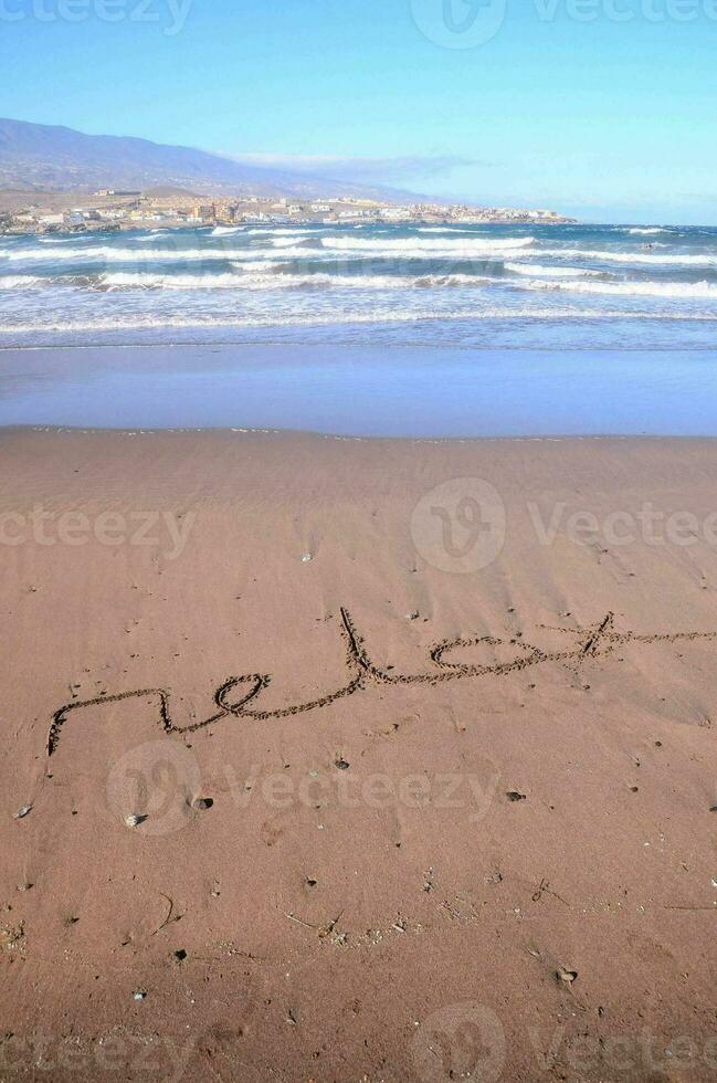 the word relax written in the sand on the beach photo