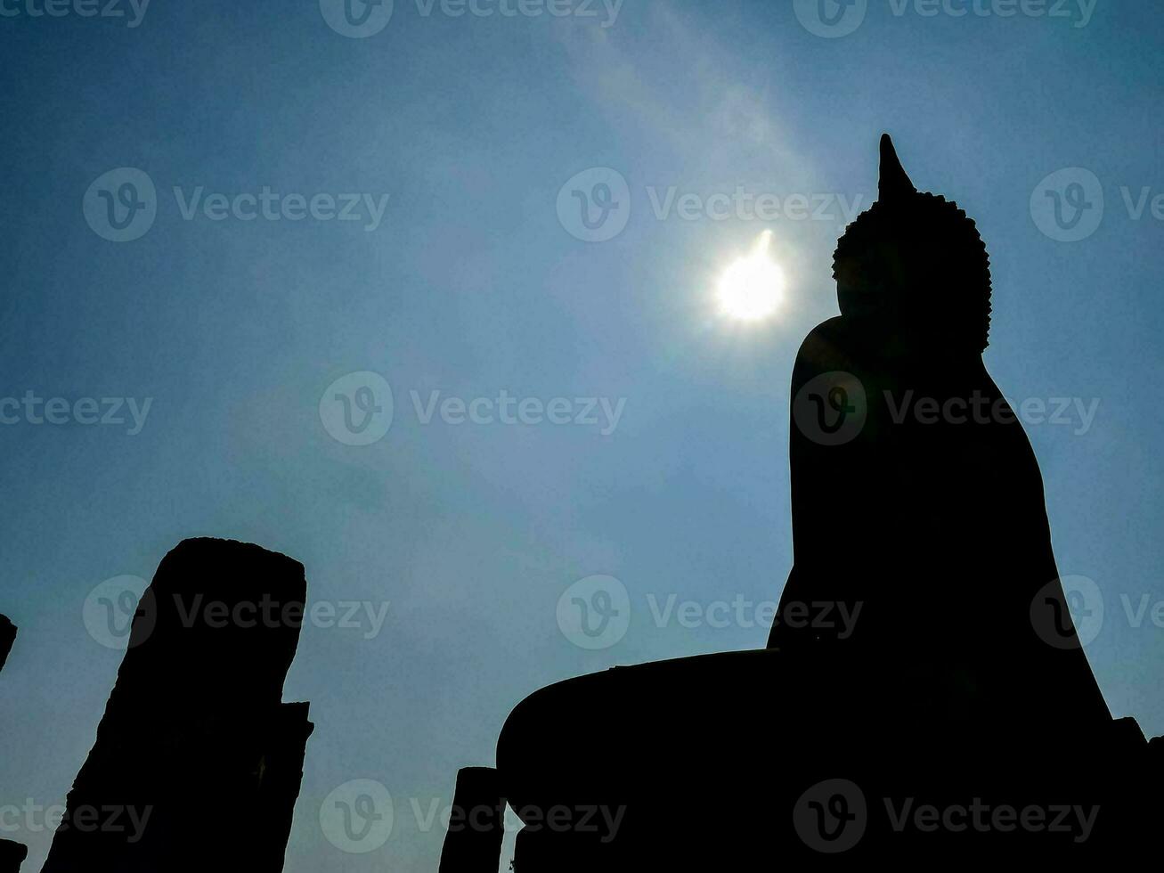 silhouette of a buddha statue in front of the sun photo