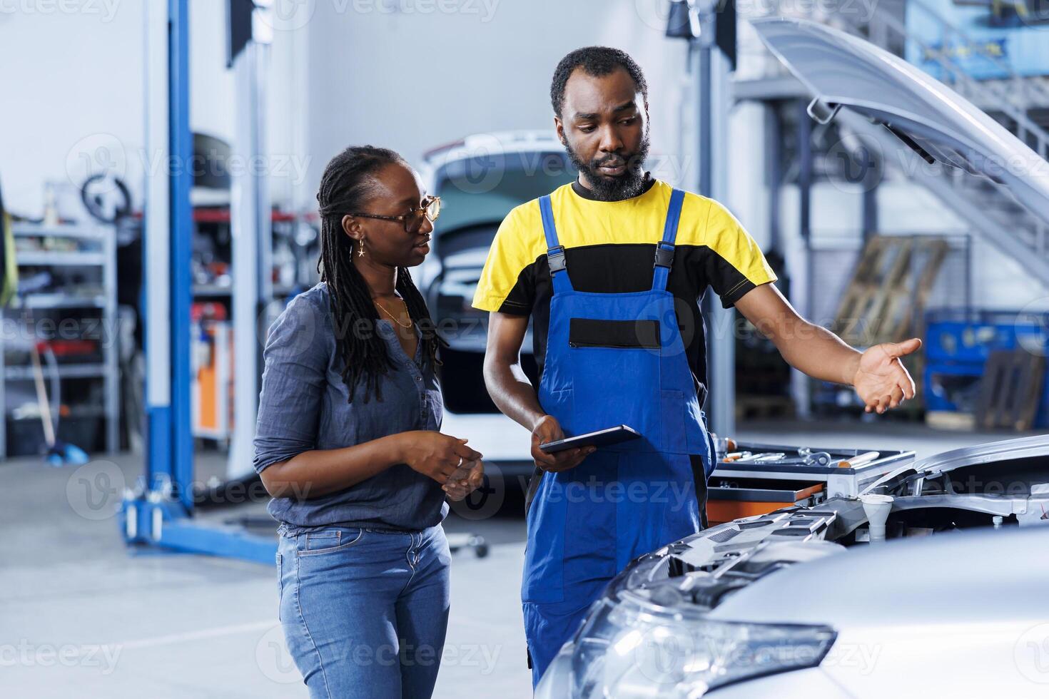 Mechanic in car service orders new compressor belt for damaged vehicle using tablet. Trained technician next to customer looking online for components to replace old ones in malfunctioning automobile photo