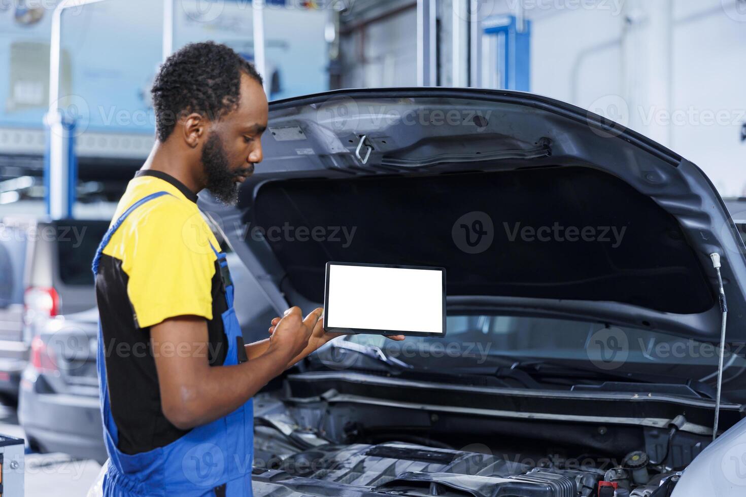 African american mechanic trainee uses mockup tablet in car service to watch tutorial on how to replace motor. Garage workplace intern looks up training videos online on isolated screen device photo