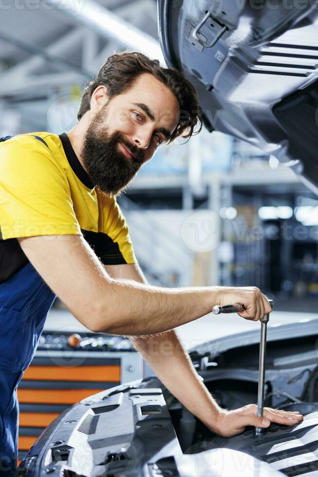 Portrait of smiling repairman in car service uses torque wrench to tighten bolts after replacing steering mechanism. Happy auto repair shop worker uses professional tools to fix customer automobile photo