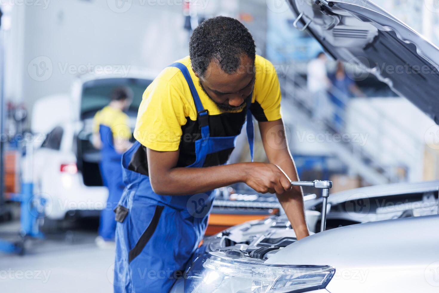 Engineer expertly examines car wheels using advanced mechanical tools, ensuring optimal automotive performance and safety. BIPOC trained garage employee conducts annual vehicle checkup photo