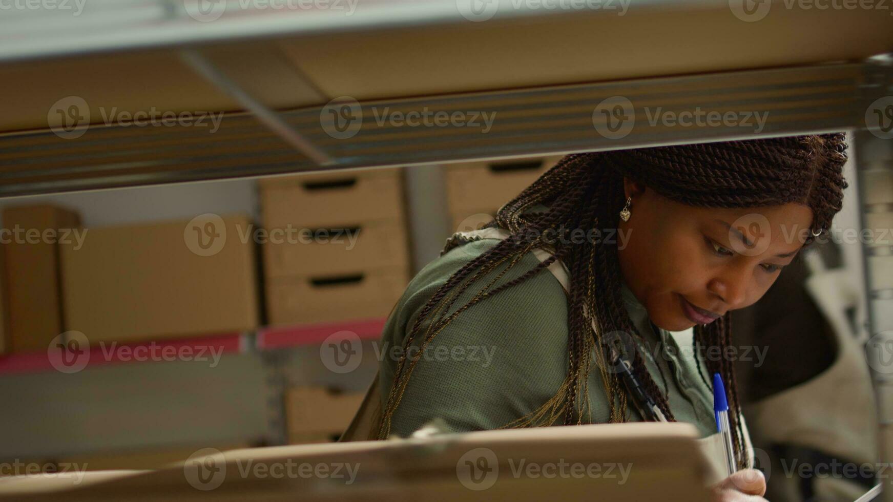 Close up shot of meticulous african american warehouse worker scanning cardboard boxes on shelves, updating merchandise labels info before sending parcels to be dispatched photo