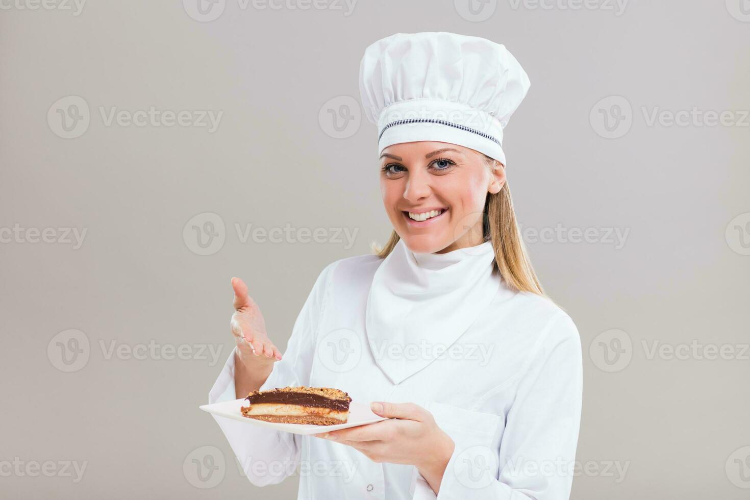 Beautiful female confectioner is showing slice of cake on gray background. photo