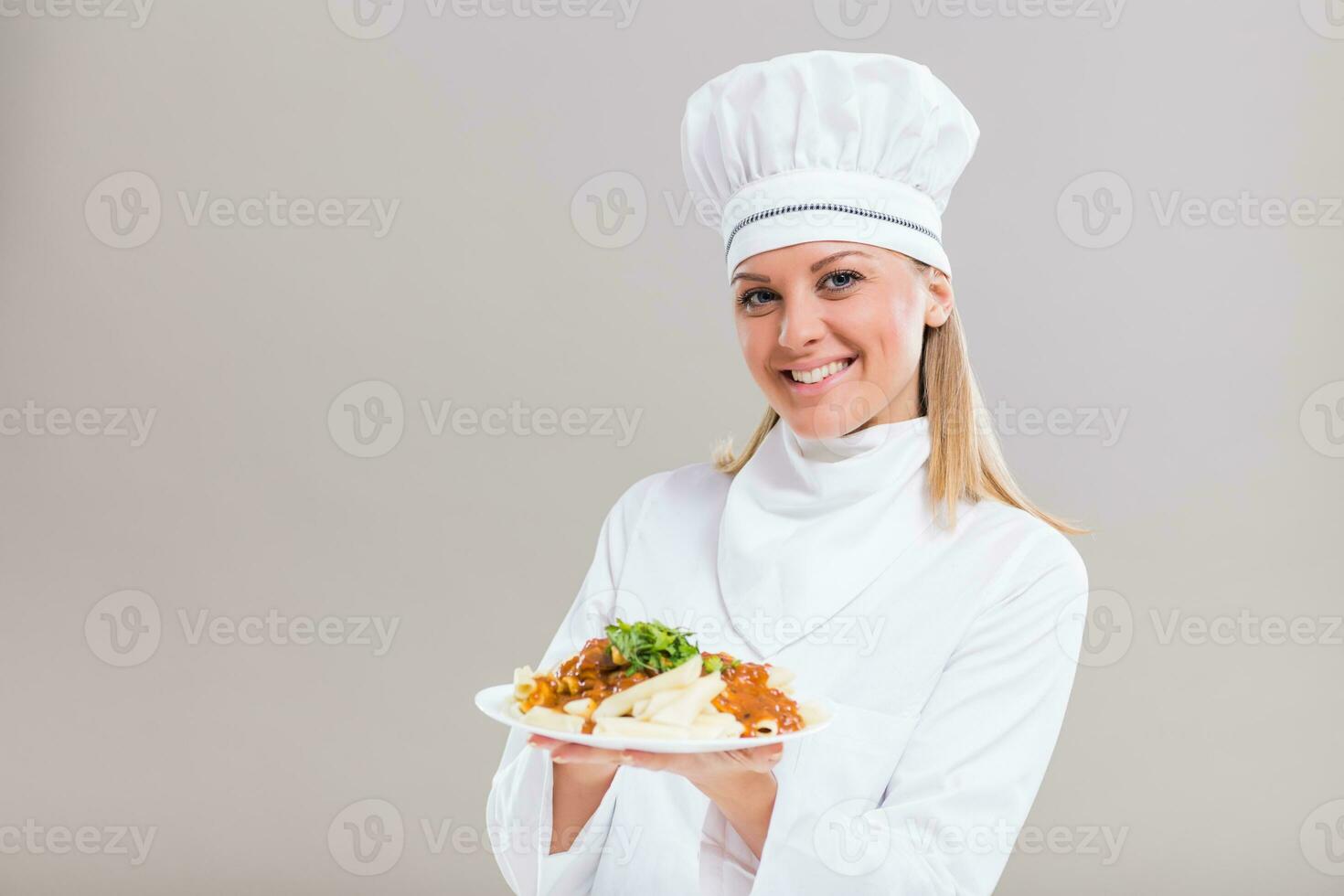 Beautiful female chef is showing prepared meal on gray background. photo