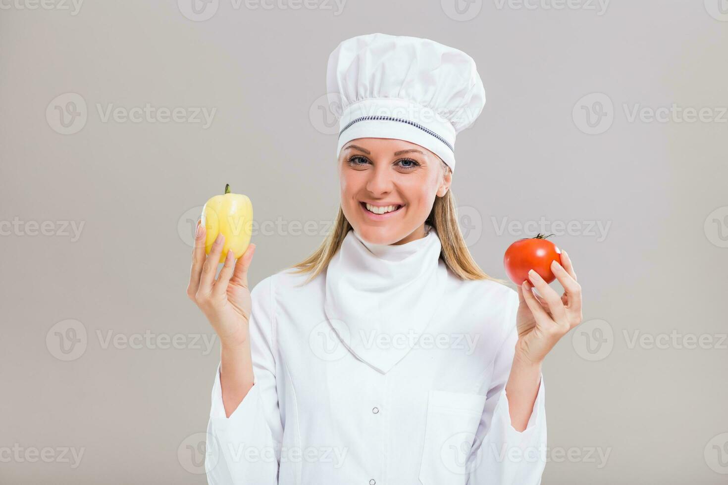 Beautiful female chef is showing vegetables on gray background photo