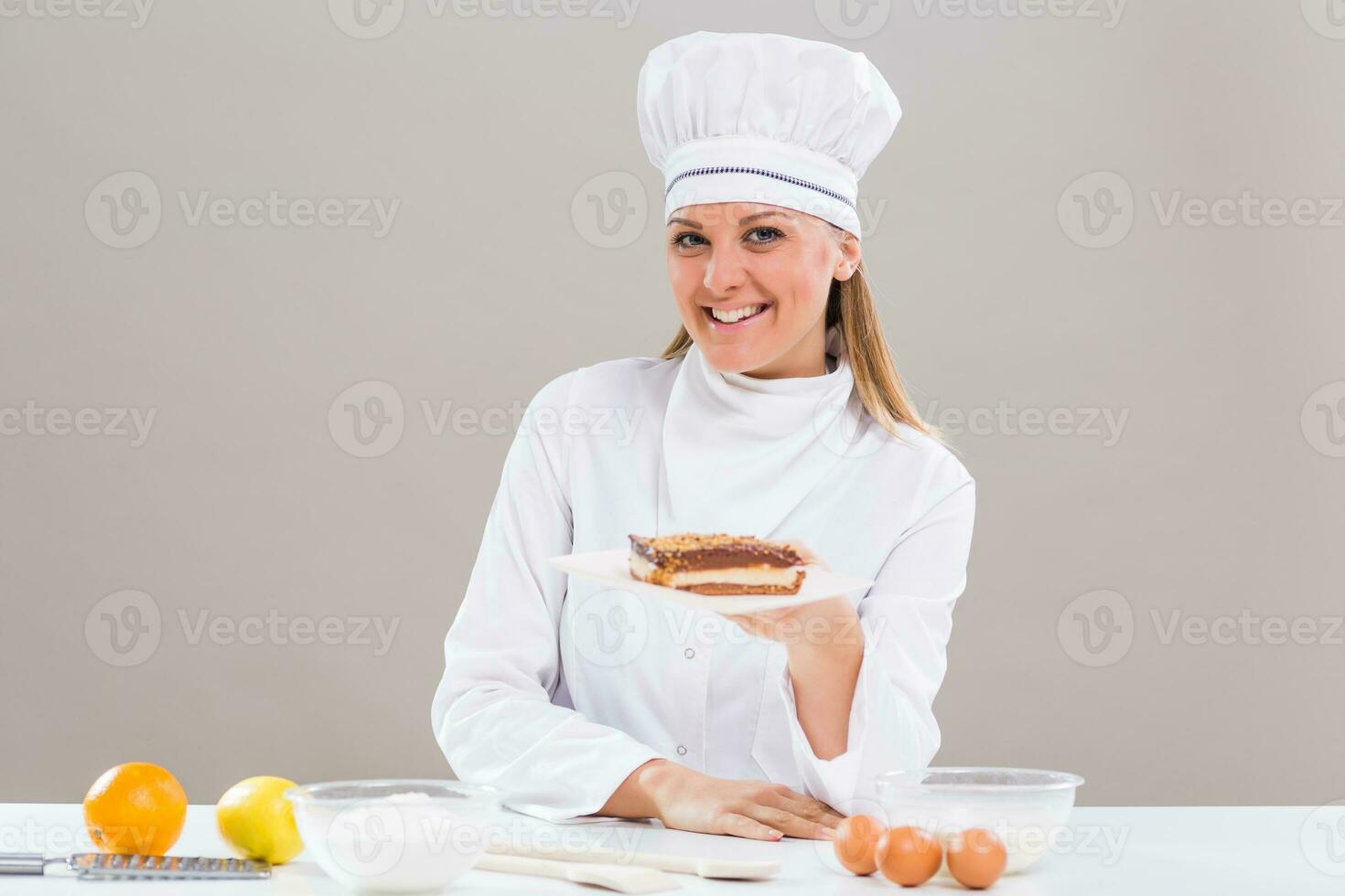 Beautiful female confectioner is showing slice of cake while sitting at the table photo