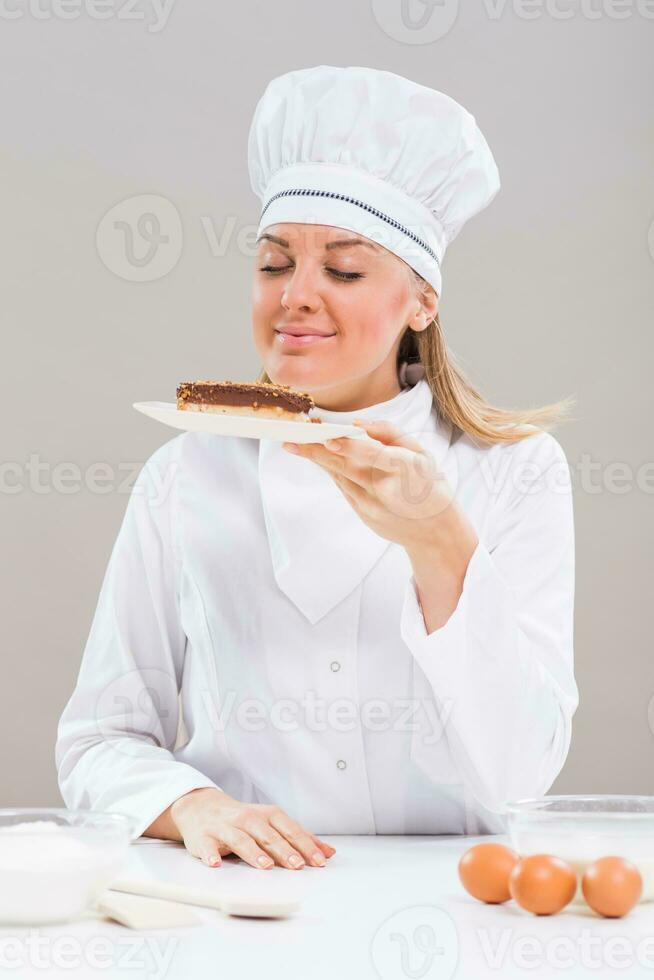 Beautiful female chef has made delicious cake and she is smelling it. photo