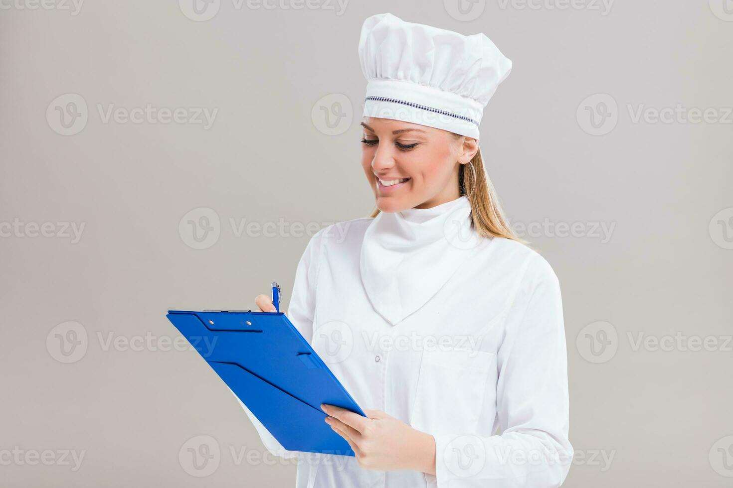 Beautiful female chef is holding cookbook and writing a new recipe. photo