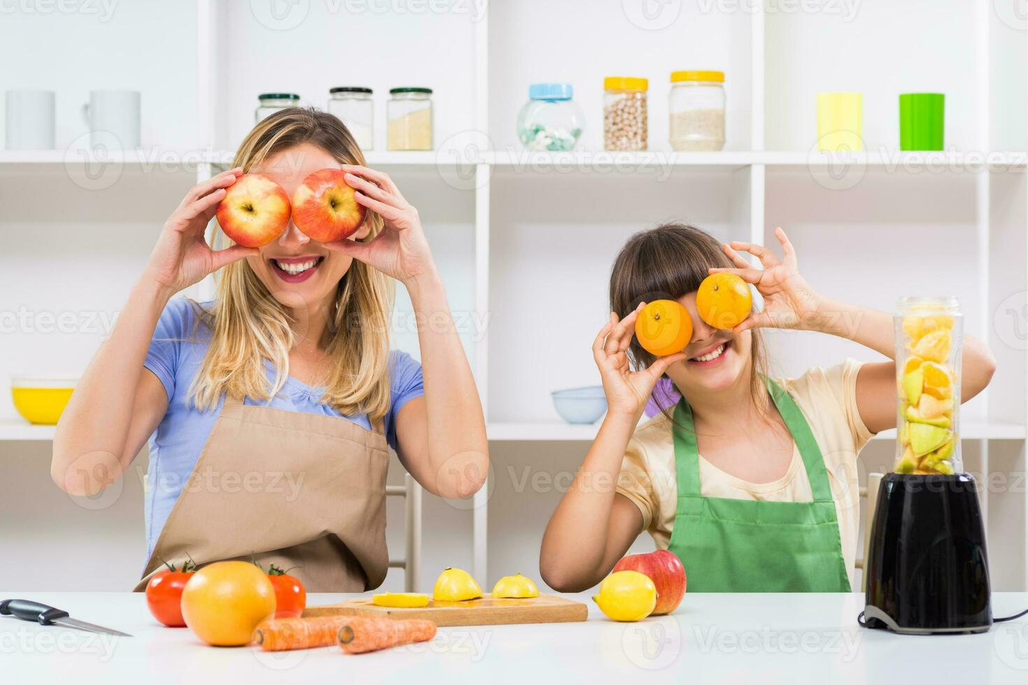 Happy mother and her daughter having fun while making smoothie together at their home. photo